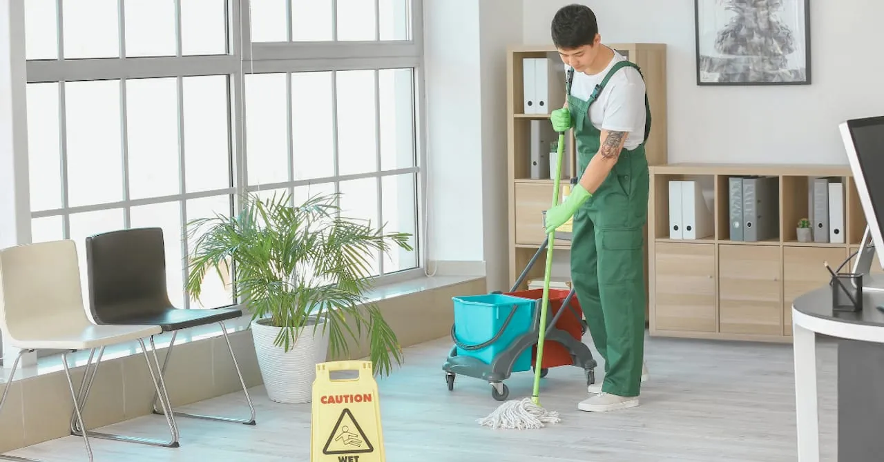 Cleaner mopping hardwood floors in an office next to a yellow wet floor caution sign