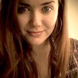 Close-up portrait of a woman with long brown hair, brown eyes, and a subtle smile, wearing hoop earrings and a plaid shirt.
