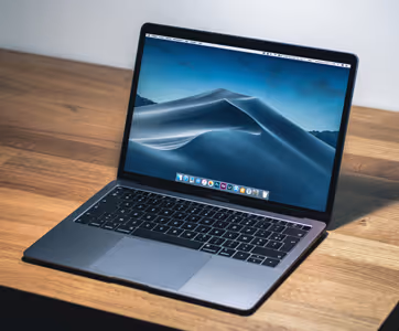 Open laptop displaying a dark scenic desert wallpaper, placed on a wooden surface.