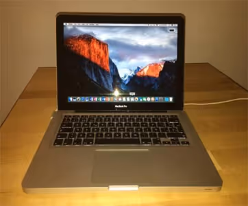 Open MacBook Pro laptop displaying a mountain wallpaper on a wooden table.