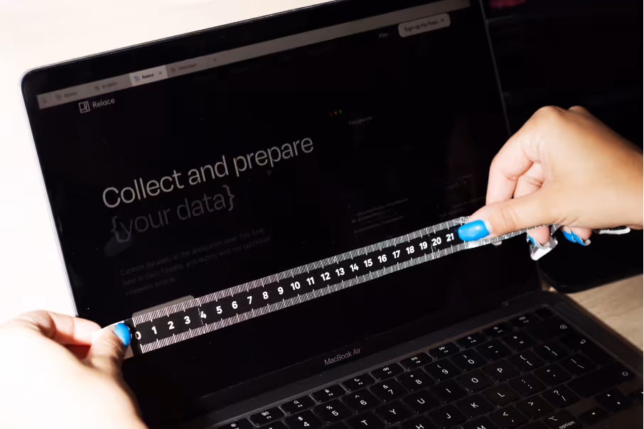 Hands with blue nail polish holding a black ruler in front of a MacBook Air screen displaying text.