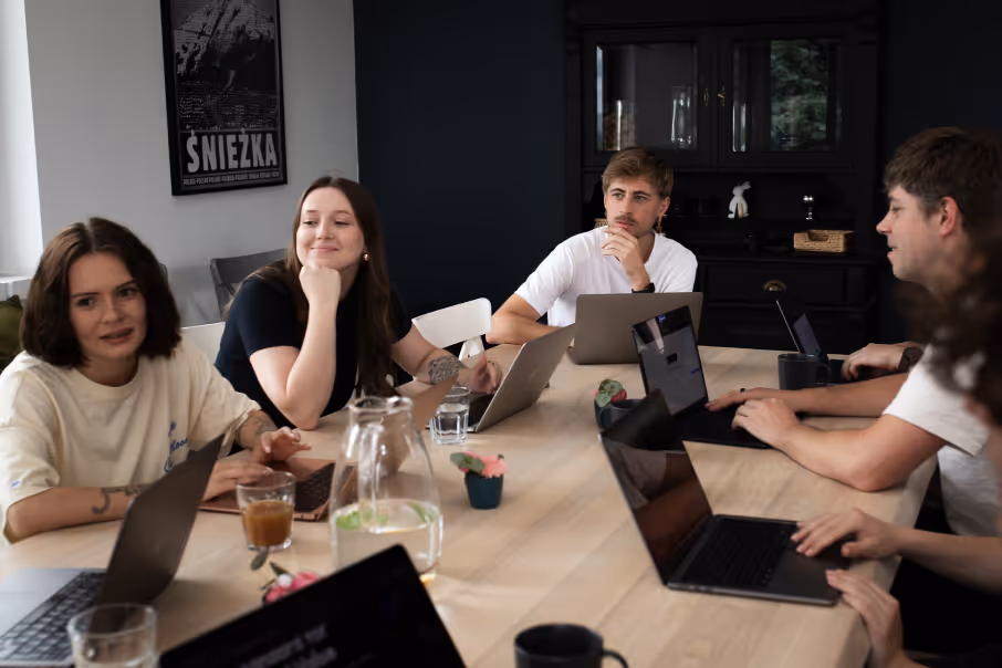 Group of young people engaged in a meeting around a table with laptops and drinks.