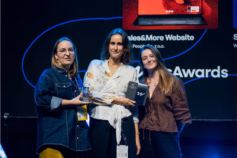 Three women standing on stage holding awards, with a presentation screen behind them.
