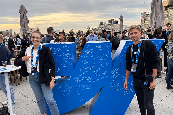 Two people standing in front of a large blue WEBNOMADS sign with handwritten messages at an outdoor event with a crowd in the background.