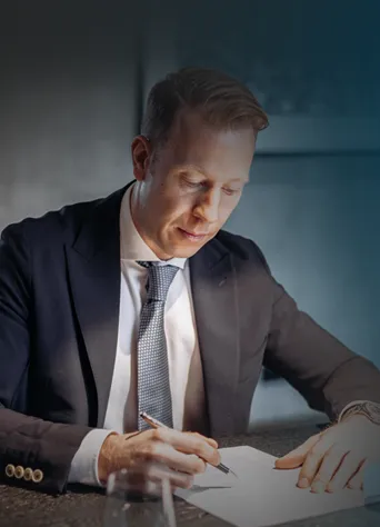 Geschäftsmann im Anzug sitzt an einem Tisch und unterschreibt ein Dokument.