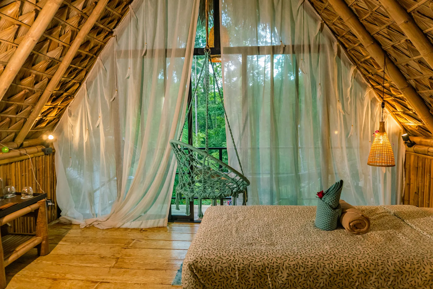 Mansard room with thatched roof, sheer curtains and hanging chair overlooking jungle