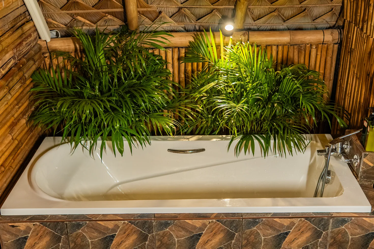 Bathtub surrounded by tropical plants and bamboo walls