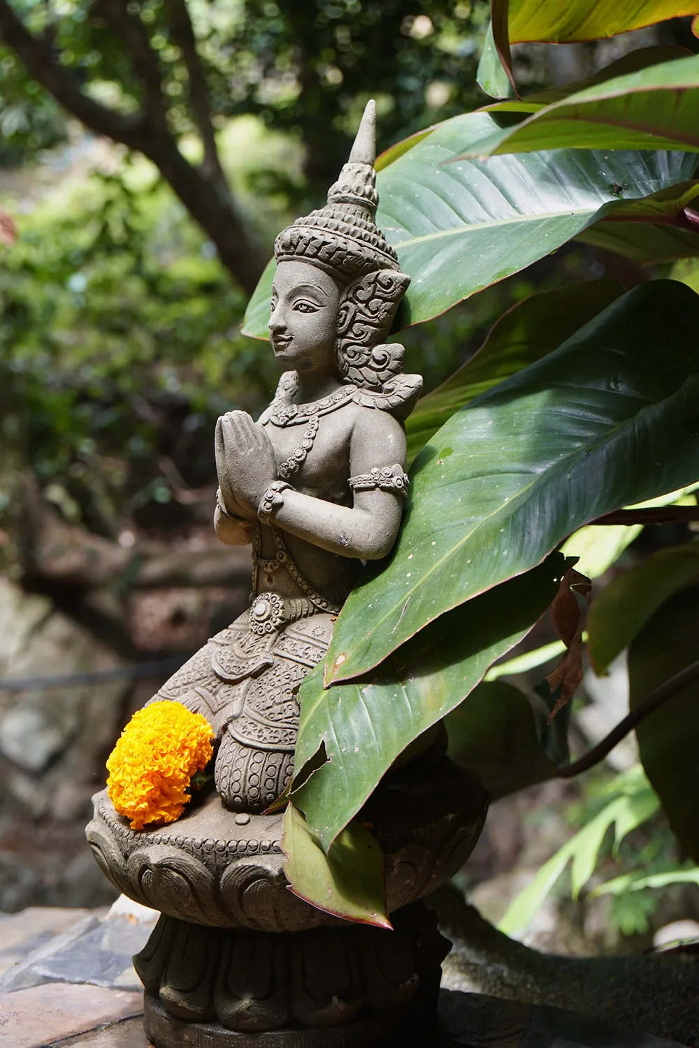 Stone statue with prayer hands among tropical leaves