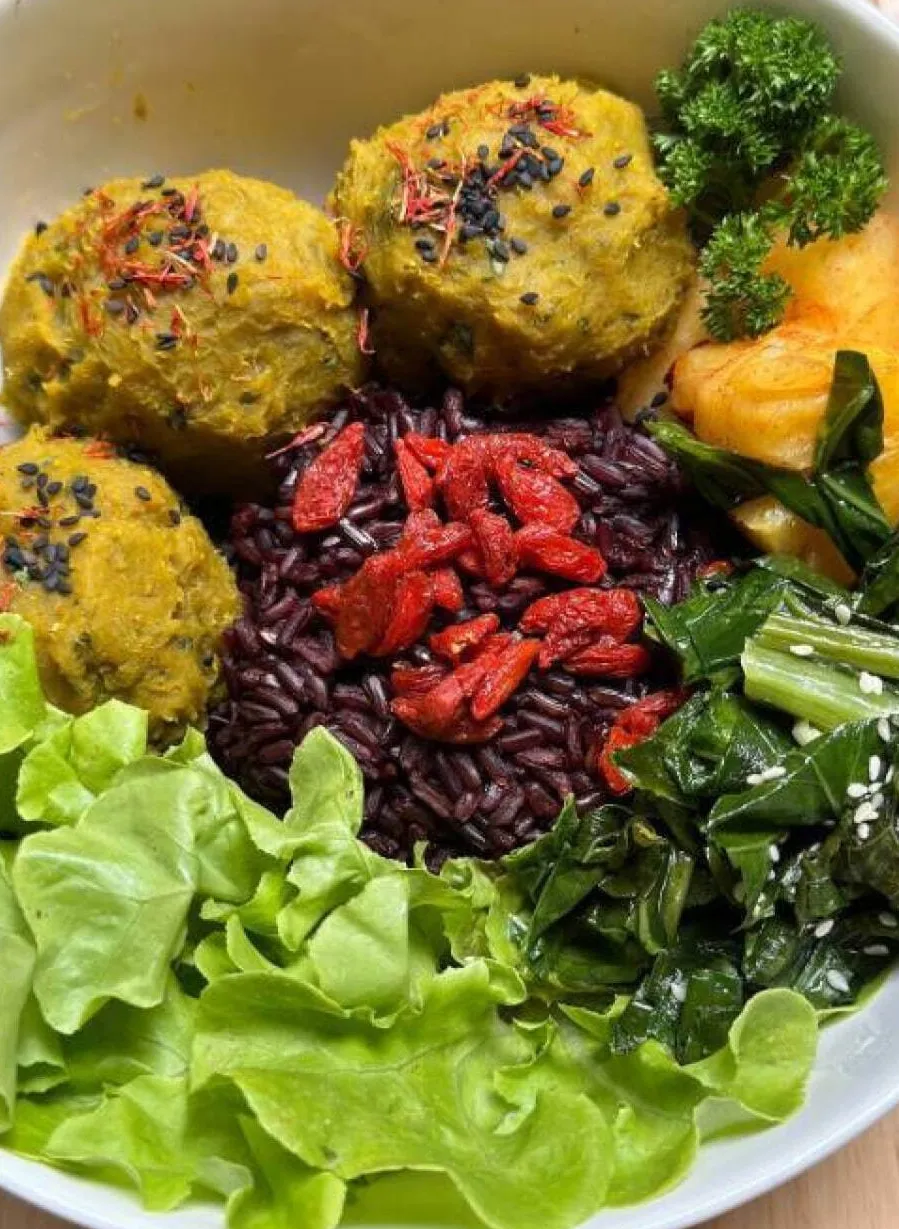 Colorful raw food plate with yellow balls, black beans, goji berries and fresh vegetables