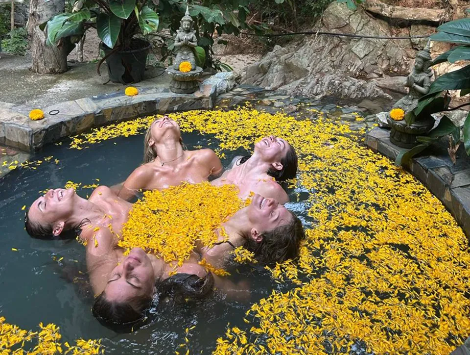 Guests relaxing in natural pool with yellow flowers by the river and waterfall