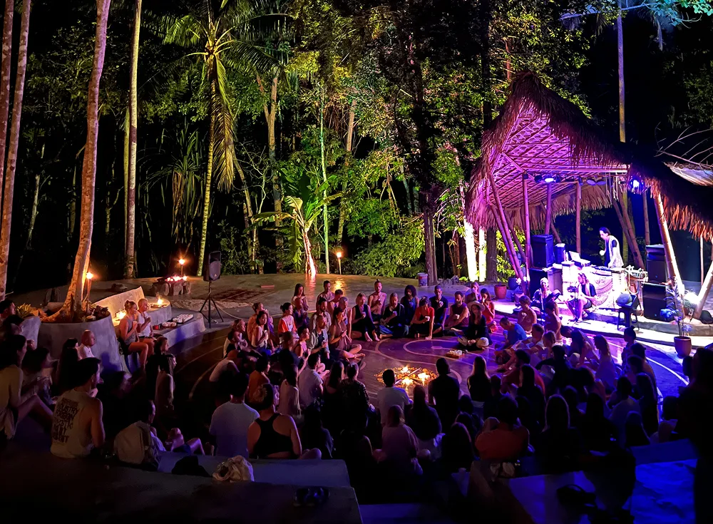 Evening gathering with live music and purple lighting in jungle pavilion