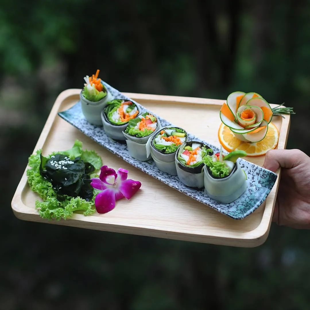 Wooden tray with raw vegan sushi rolls decorated with fresh vegetables and orchid flower for detox program