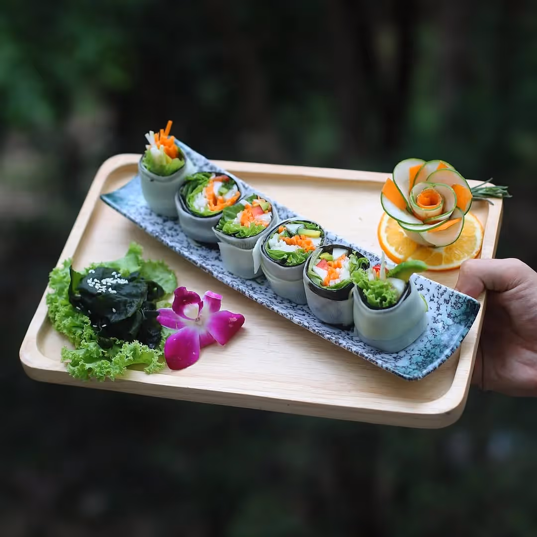 Raw vegan sushi rolls with vegetables and decorative flower garnish on wooden tray