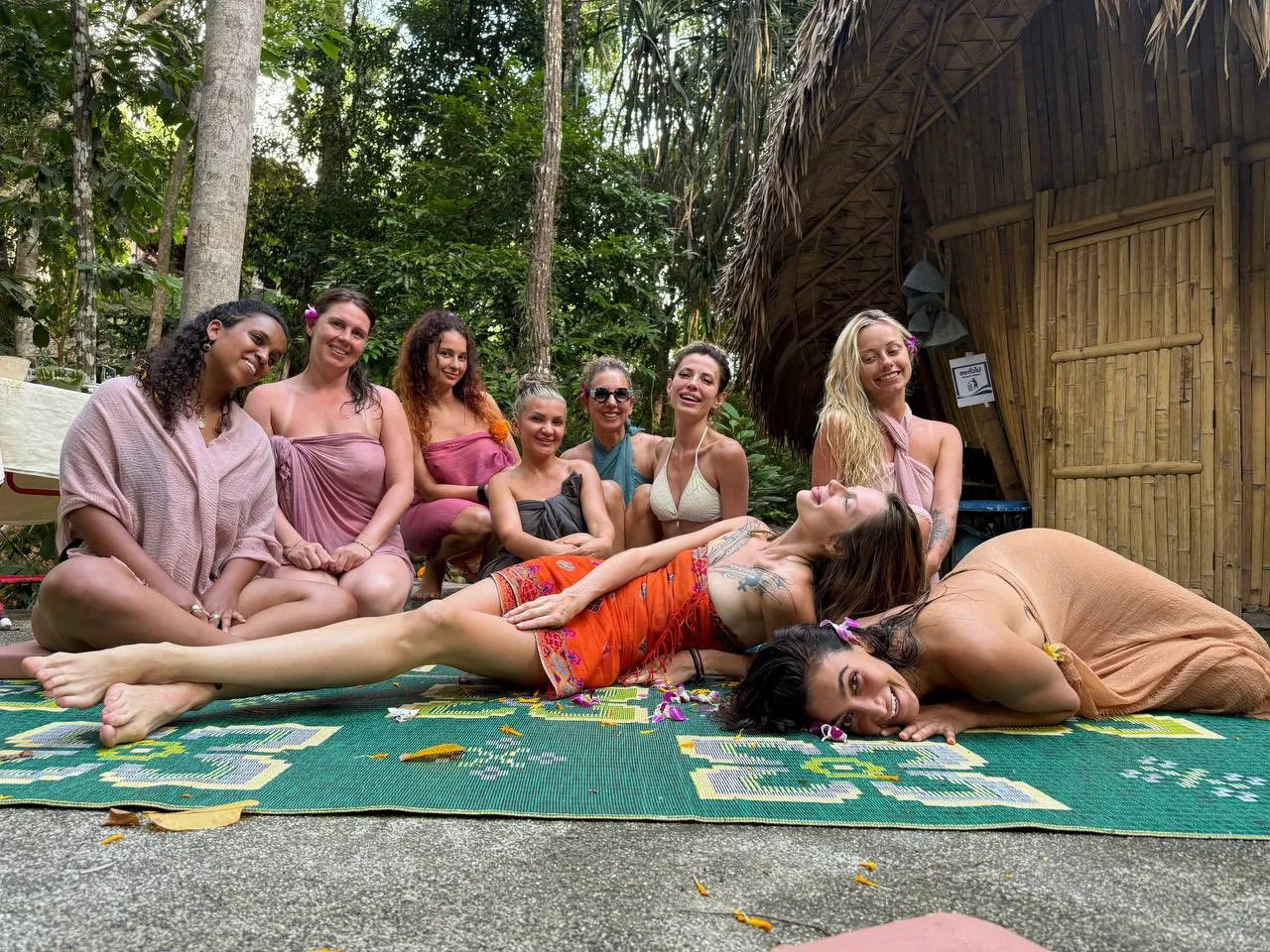 Group of women relaxing on yoga mats in jungle setting after wellness retreat session