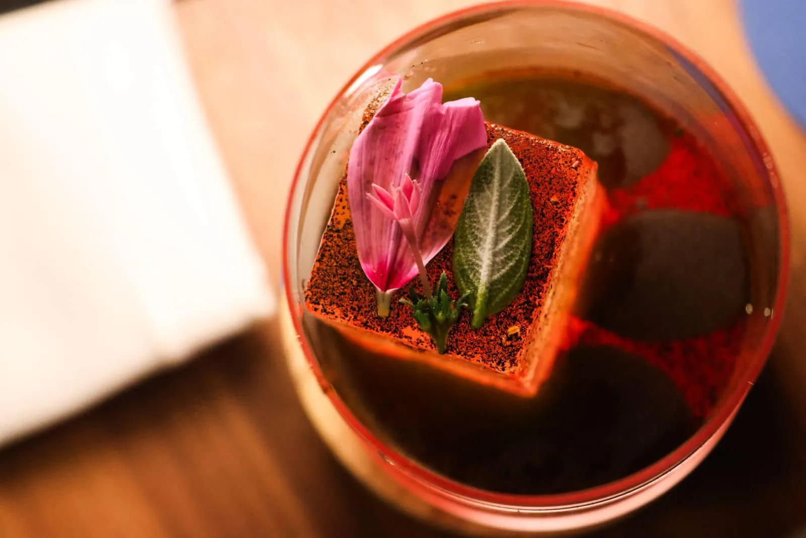 Cocktail ambré garni d'un glaçon épicé, d'un pétale et d'une feuille fraîche