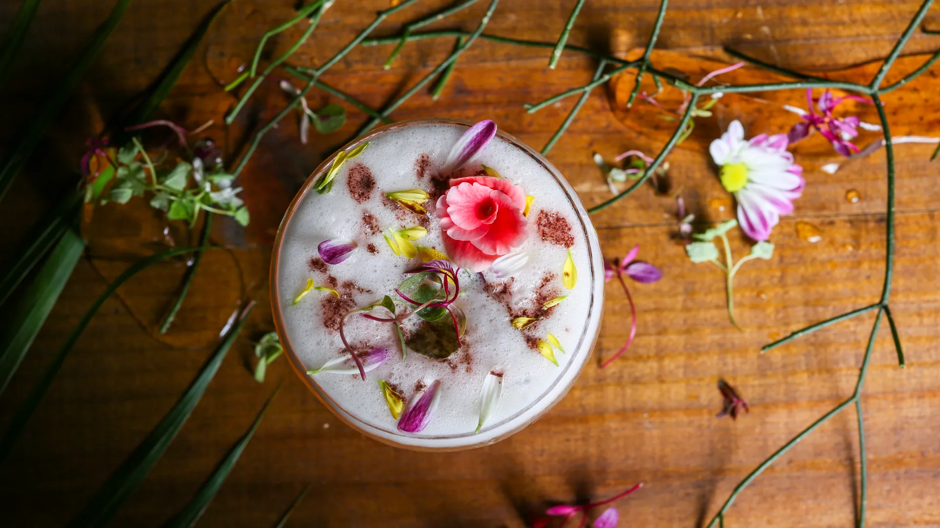 Cocktail aux fleurs comestibles vu de dessus sur une table en bois