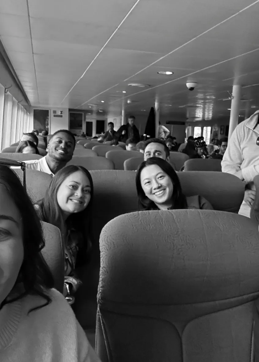 Group of smiling people sitting in rows of seats inside a bus or ferry.