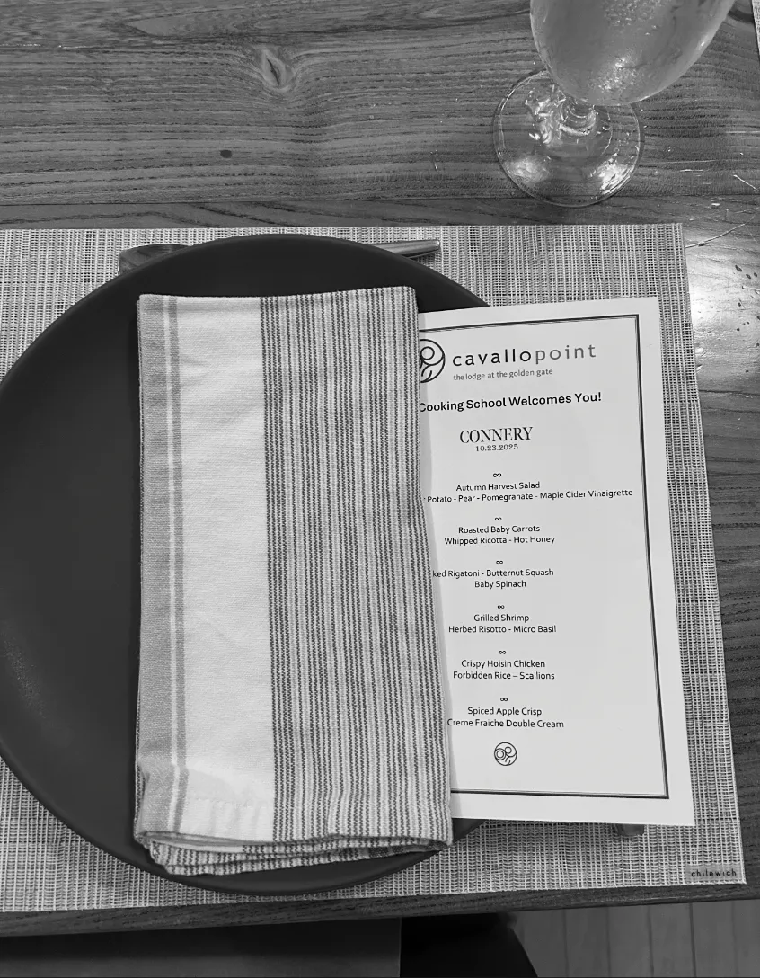 Table setting with a dark plate, striped napkin, a printed menu for connery team, and a glass of water on a wooden table.