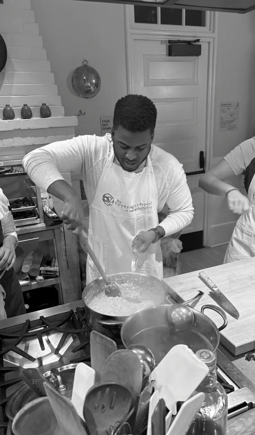 John Patterson in apron stirring food in a pot on a stove in a cooking class setting.