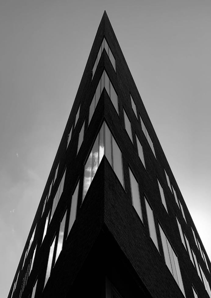 Black and white photo of a sharp-angled modern building with reflective windows taken from below.