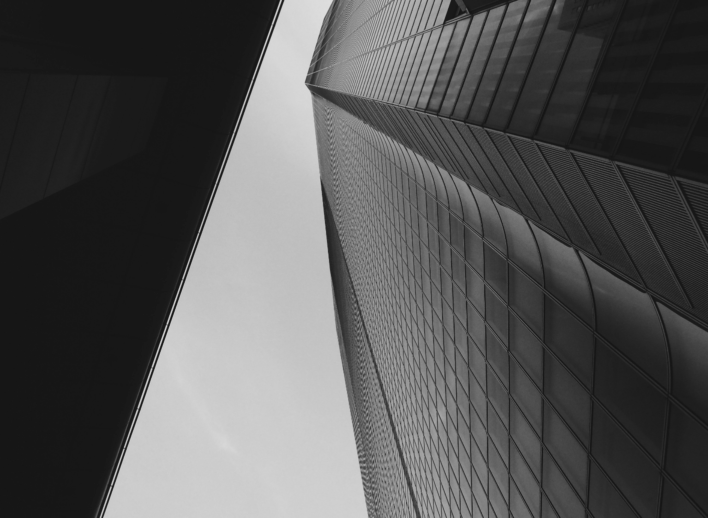 Low-angle black and white photo of two modern skyscrapers with glass facades converging towards the sky.