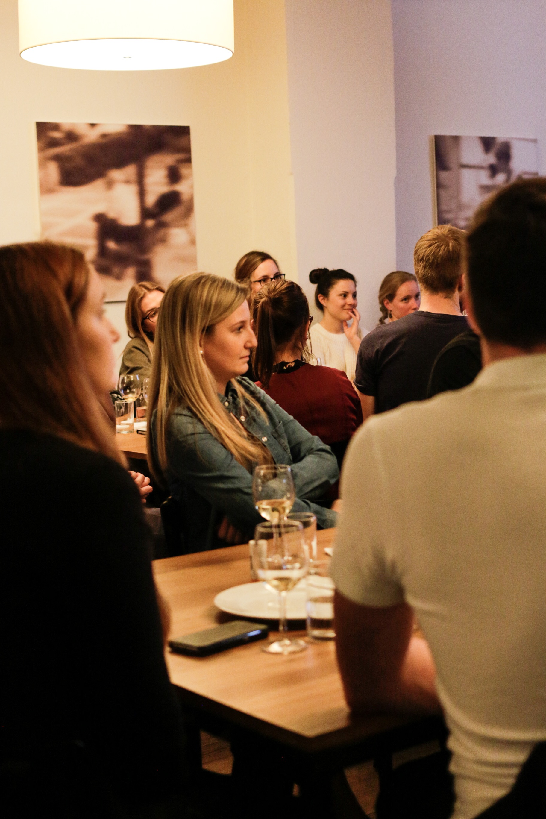Gruppe von Personen sitzt an einem Holztisch in einem gemütlichen Raum mit Getränken und Kunst an der Wand.