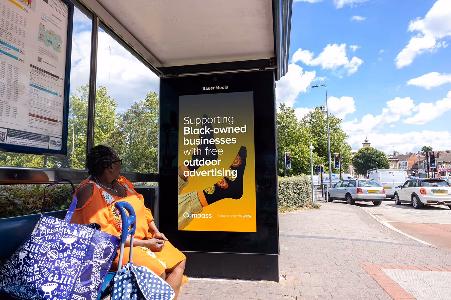 A person sitting on a Bauer Media Outdoor bus stop.