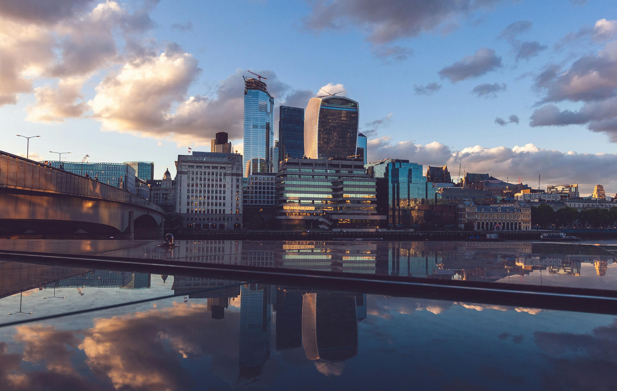 City skyline with modern skyscrapers reflecting on calm water at sunset with partly cloudy sky.