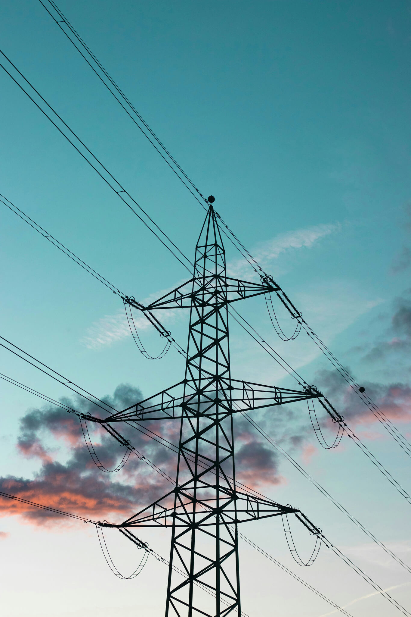 Silhouette of a high-voltage electricity transmission tower against a blue sky with pink and gray clouds at sunset.