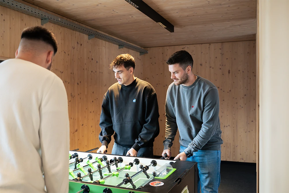 Mitarbeitende von Schröder & Partner – Beratende Ingenieure VBI für Elektrotechnik spielen gemeinsam Tischkicker im Aufenthaltsbereich.