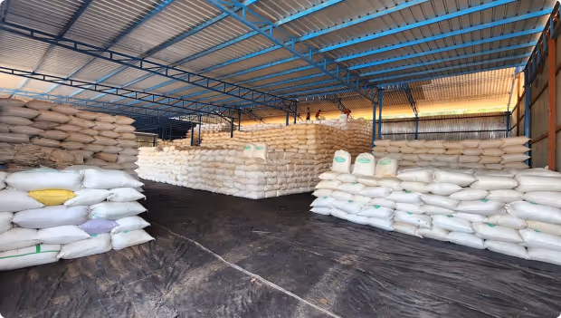 Warehouse interior with large stacks of white and beige sacks neatly piled under a blue metal roof.