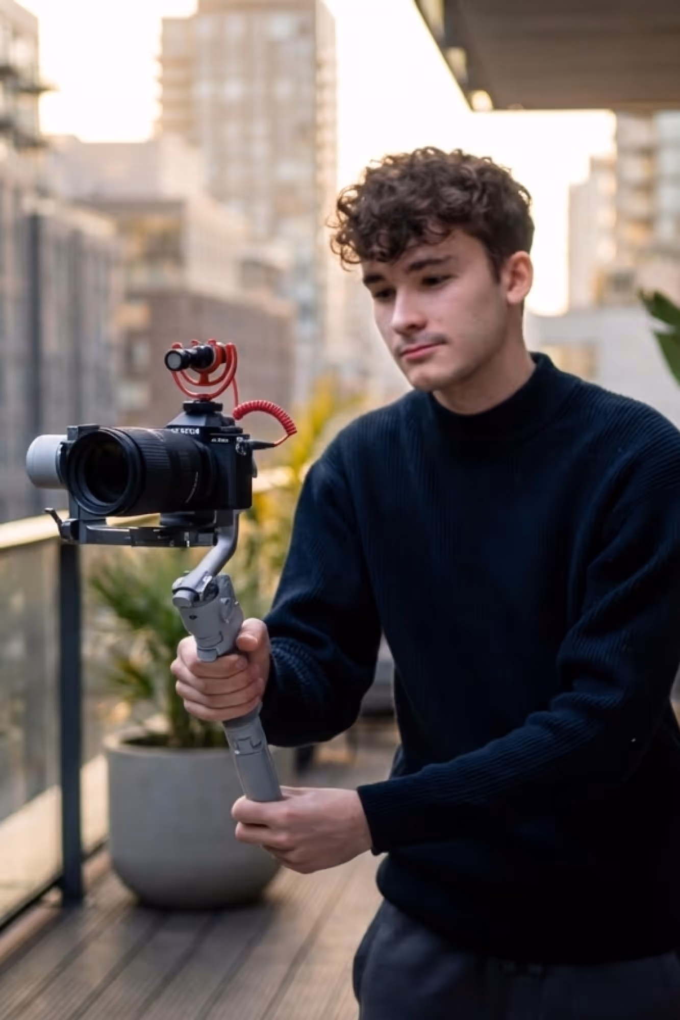 Junger Mann auf einem Balkon hält eine Kamera mit Mikrofon an einem Gimbal-Stabilisator.