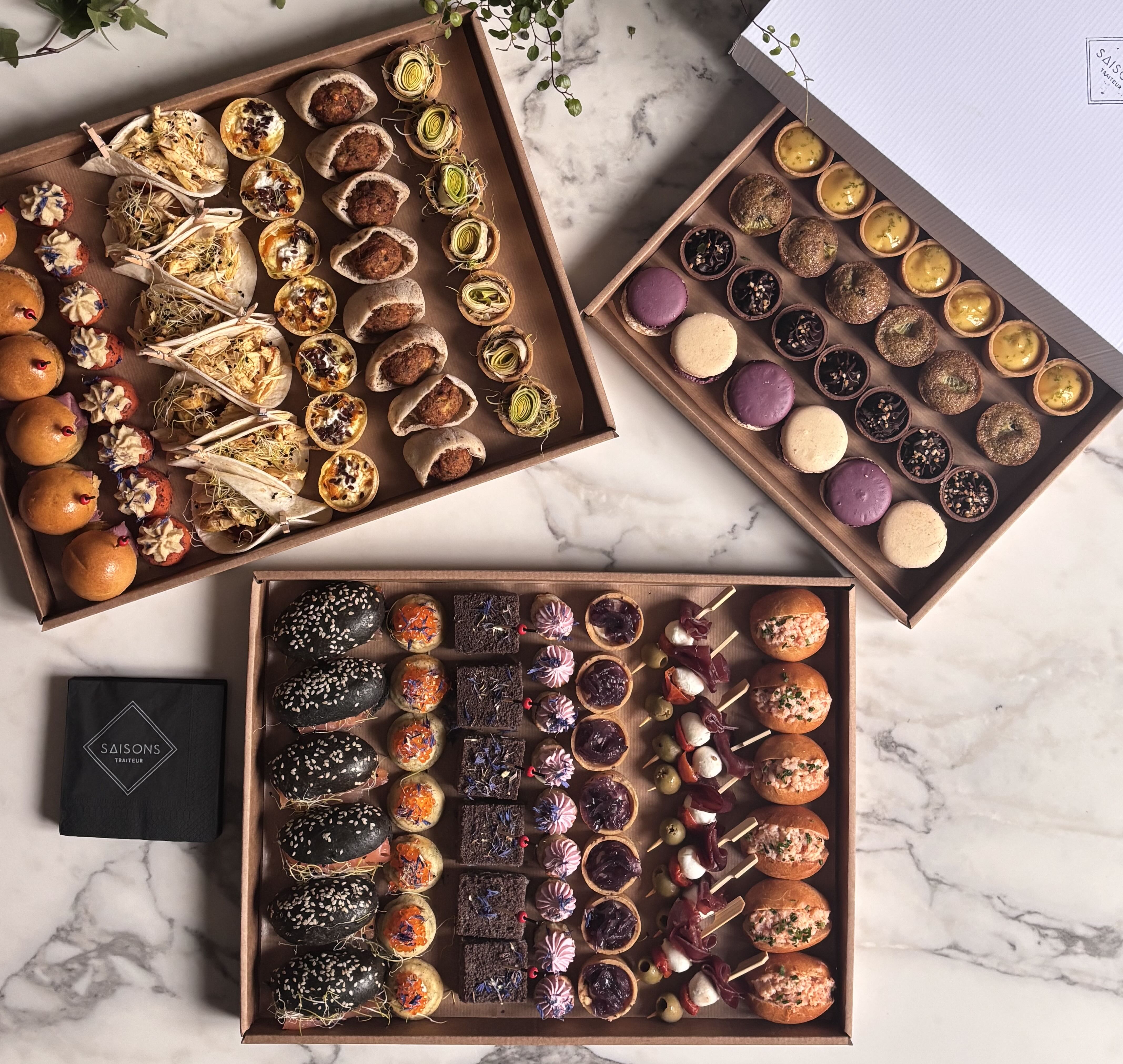 Trois plateaux de bouchées apéritives variées, sucrées et salées, joliment présentées sur une table en marbre.