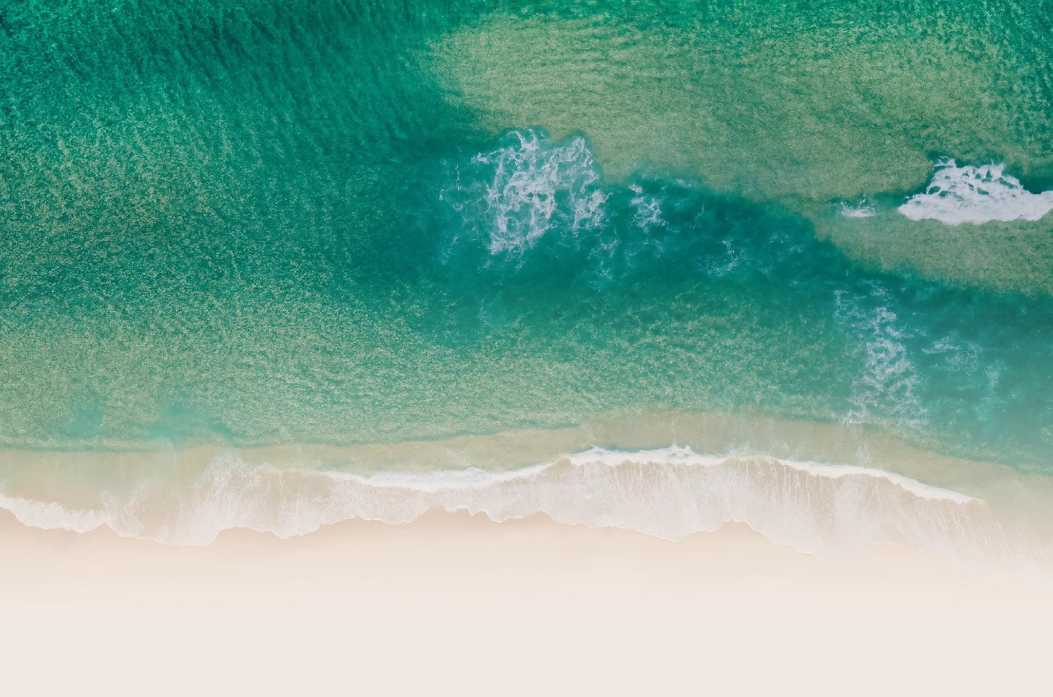 Aerial view of turquoise ocean waves gently rolling onto a sandy beach.