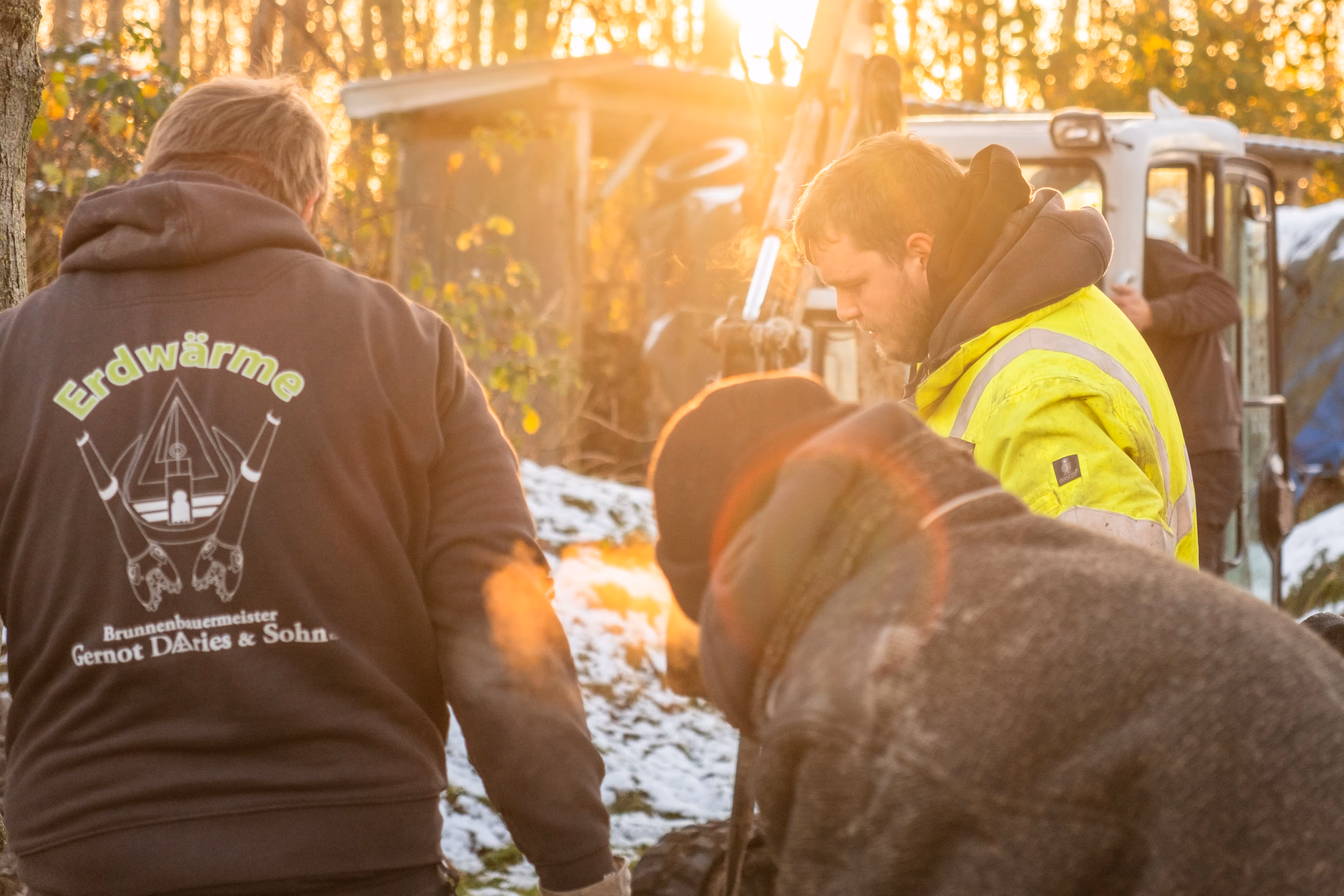 Männer in Arbeitskleidung bei Sonnenuntergang mit Ausrüstung im schneebedeckten Gelände.
