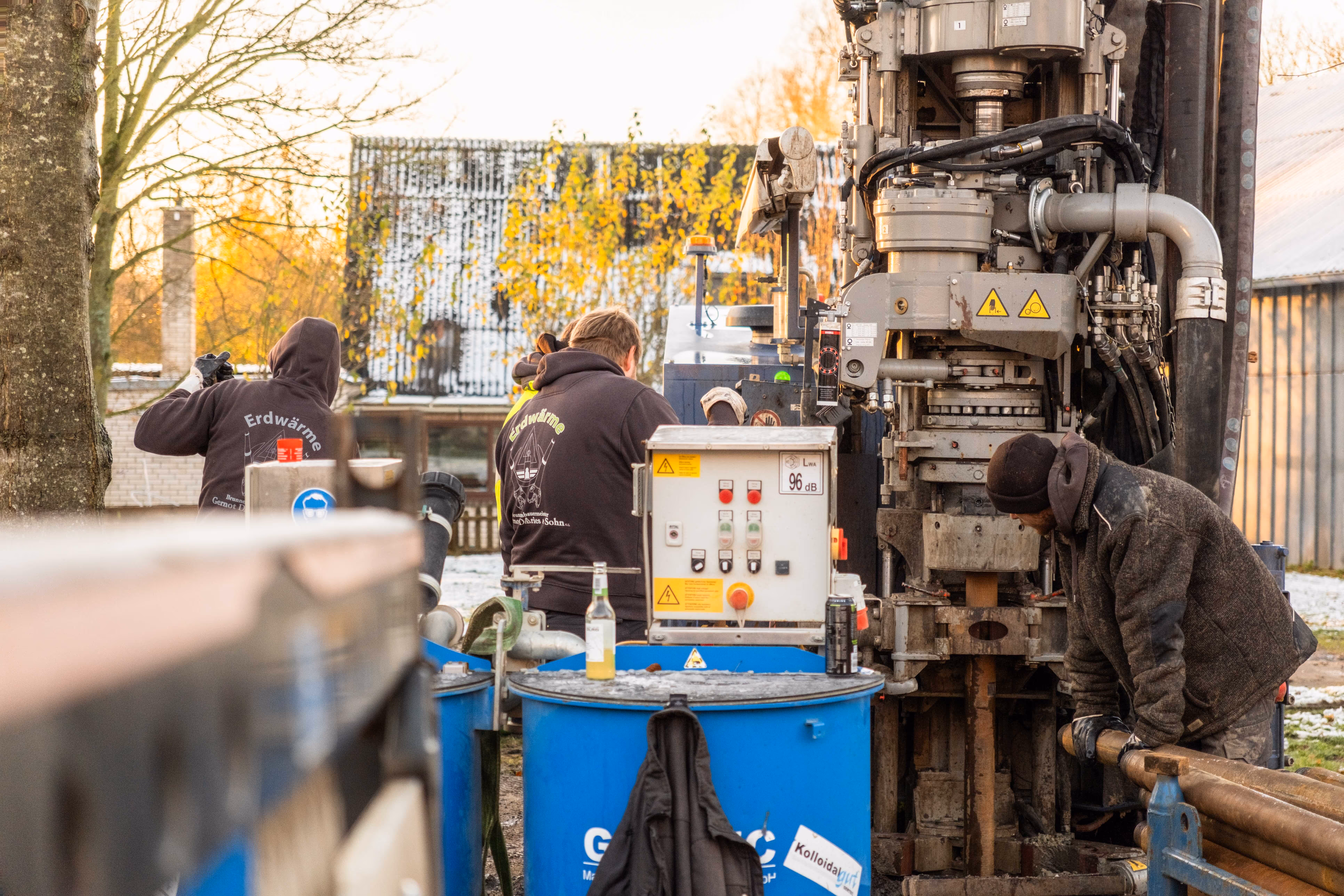 Drei Arbeiter in Jacken bedienen eine Bohrmaschine im Freien an einem Herbsttag.
