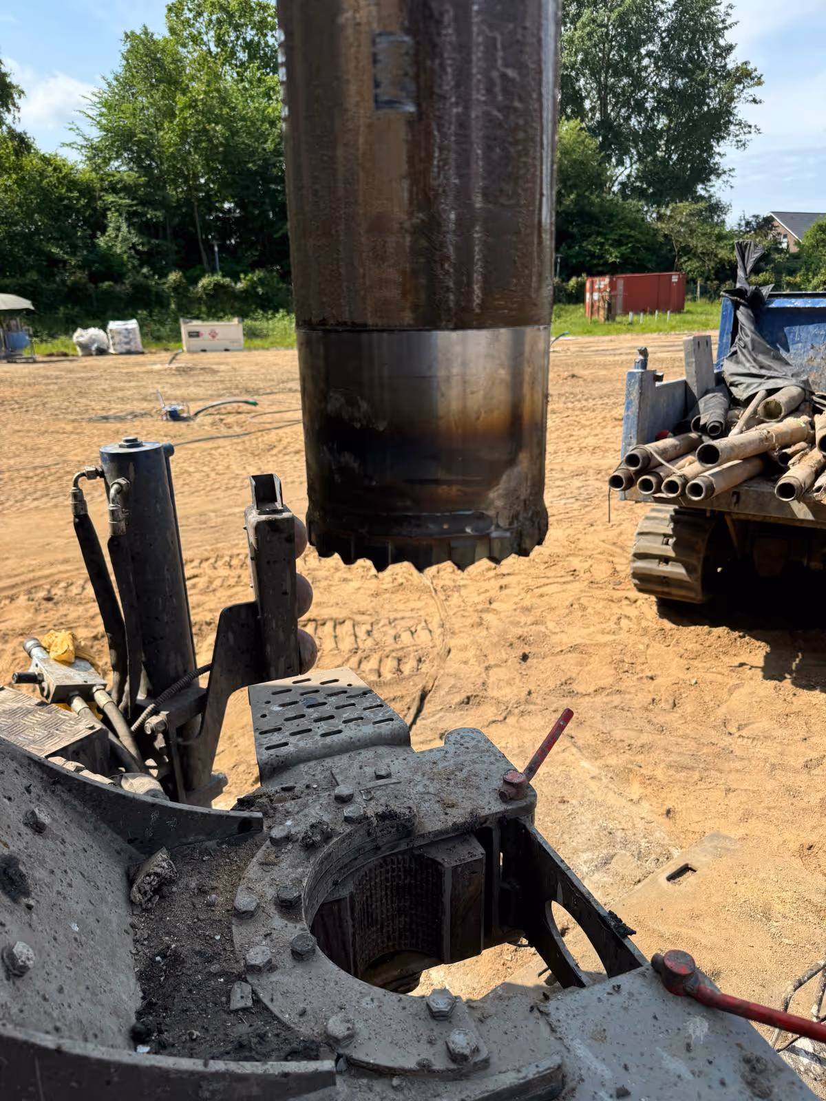 Bohrmaschine auf einer Baustelle mit einem großen Bohrkern in der Mitte und sandigem Boden im Hintergrund.