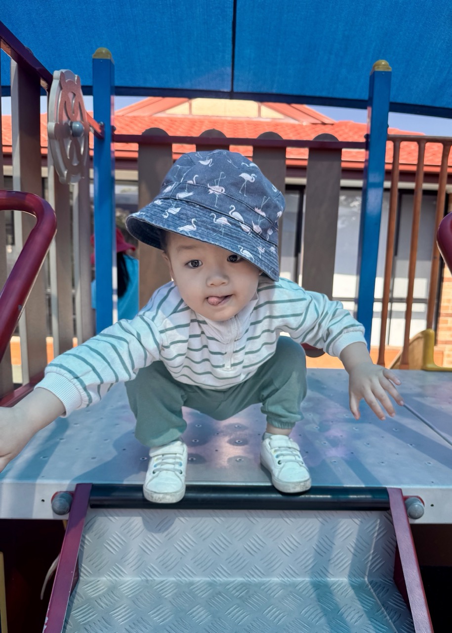 Smiling boy sitting at a classroom table with pencils and schoolwork in front of him.