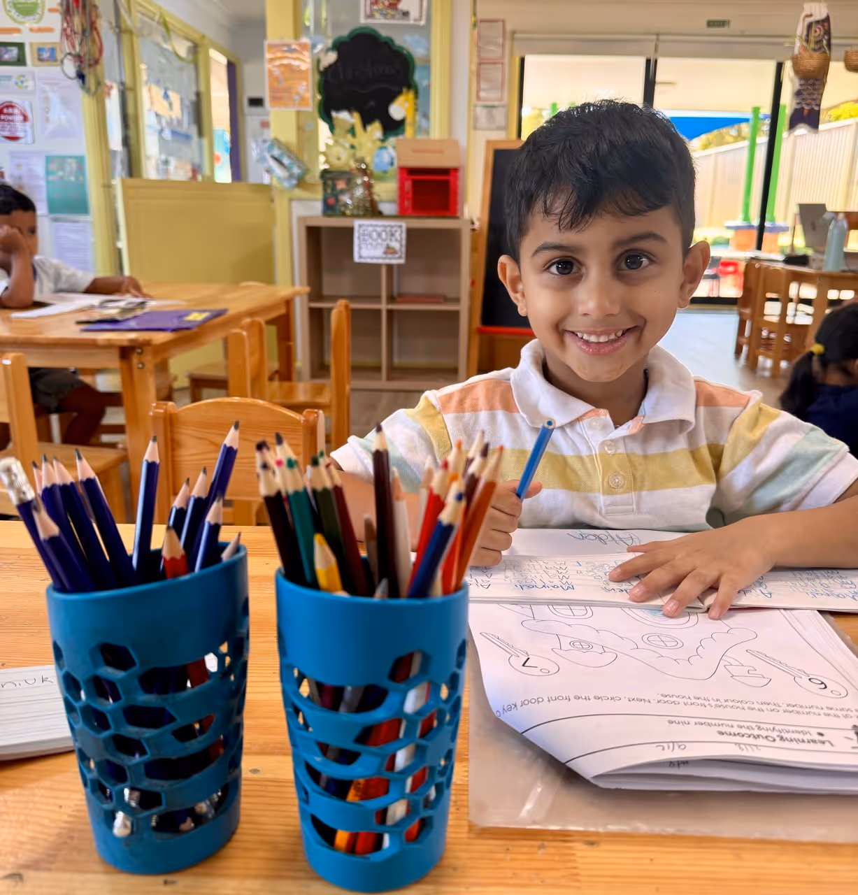 Toddler wearing a striped sweater, green pants, white shoes, and a blue flamingo-patterned hat crouching on playground equipment.