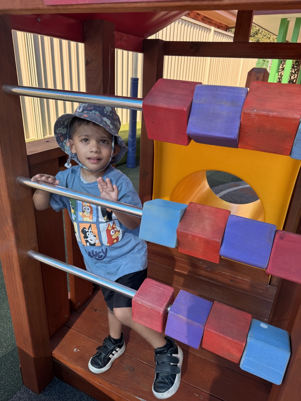Smiling boy sitting at a classroom table with pencils and schoolwork in front of him.