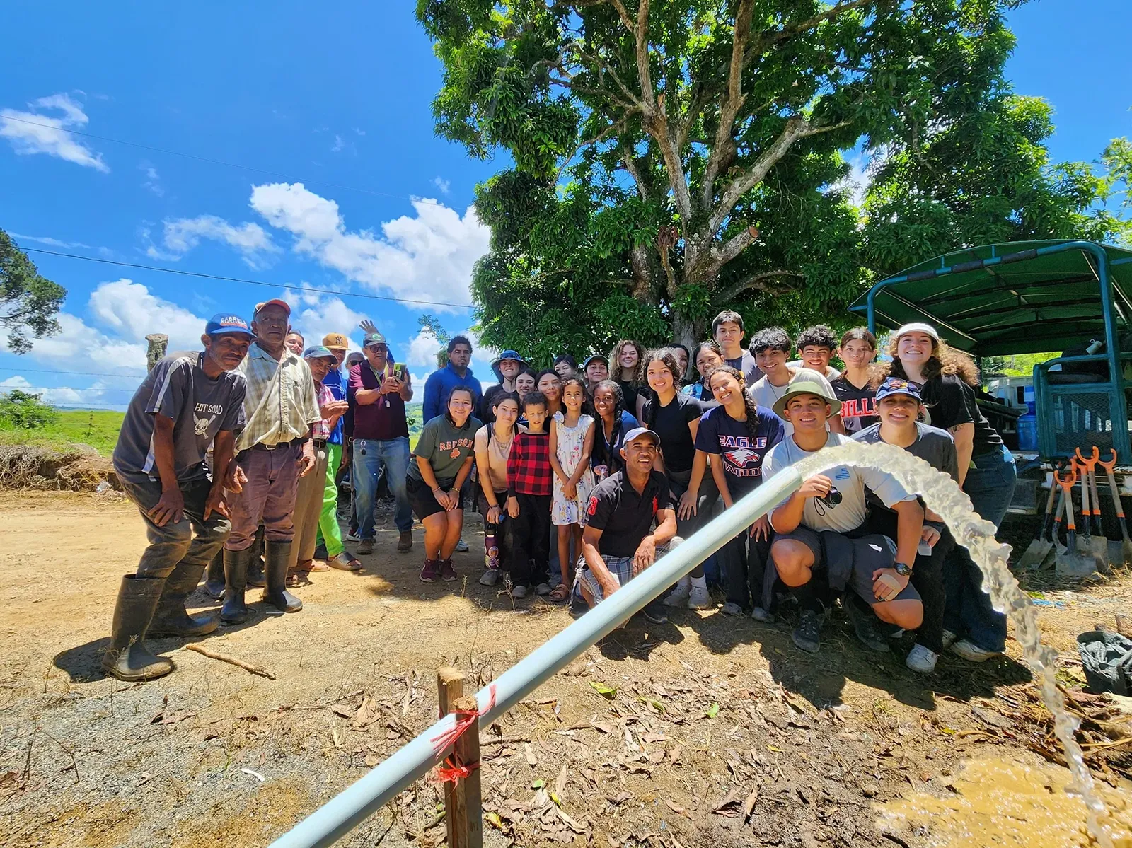 A group of people smiling and posing together outdoors near a large tree.