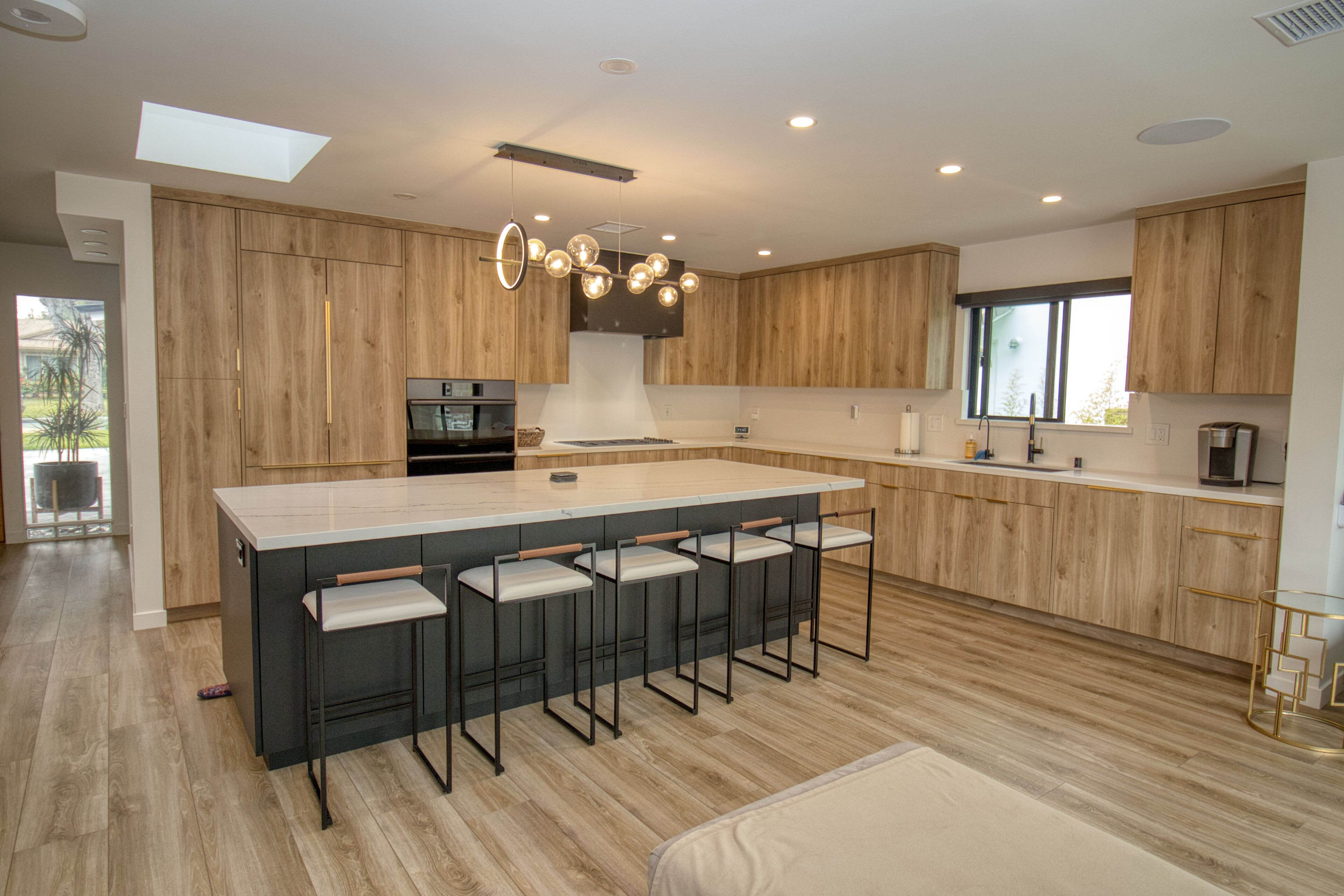 Modern kitchen with natural wood cabinets, dark green island, white countertops, stainless appliances, and hardwood floors