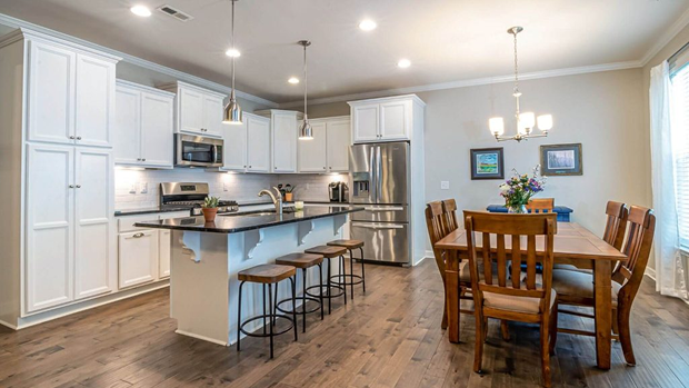 Modern white kitchen with dark countertops, stainless steel appliances, and open dining area with hardwood floors