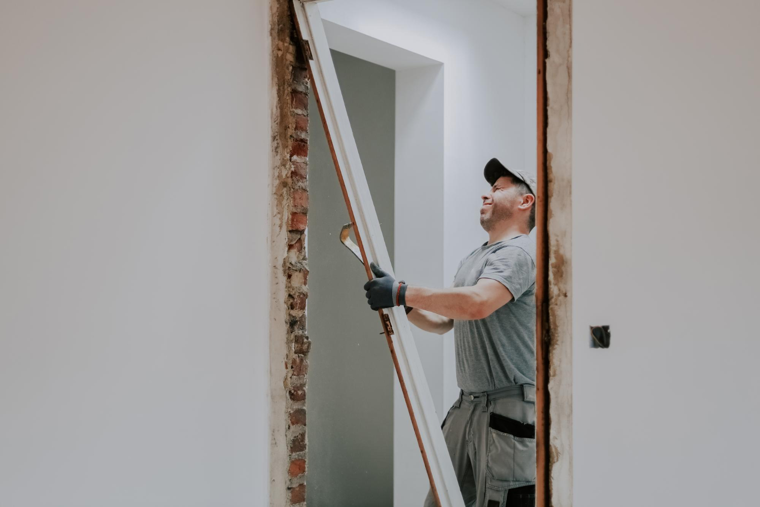 Construction worker installing white door frame in exposed brick wall opening during commercial renovation project