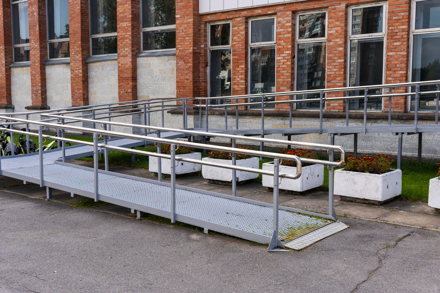 Metal wheelchair ramp with handrails leading to brick building entrance, featuring non-slip grating and ADA-compliant design