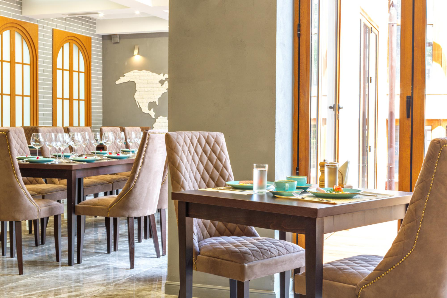 Elegant restaurant interior with quilted beige chairs, dark wood tables, arched windows, and modern lighting showcasing commercial remodeling design.