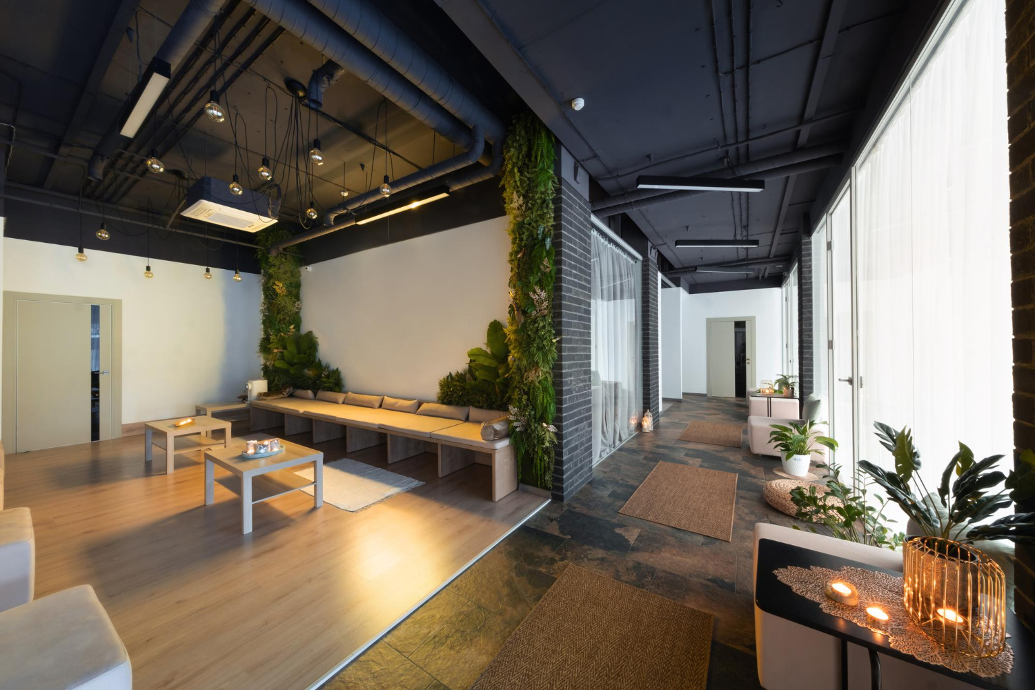 Modern office renovation with exposed black ceiling, living green wall, concrete floors, wooden seating area, and natural lighting.