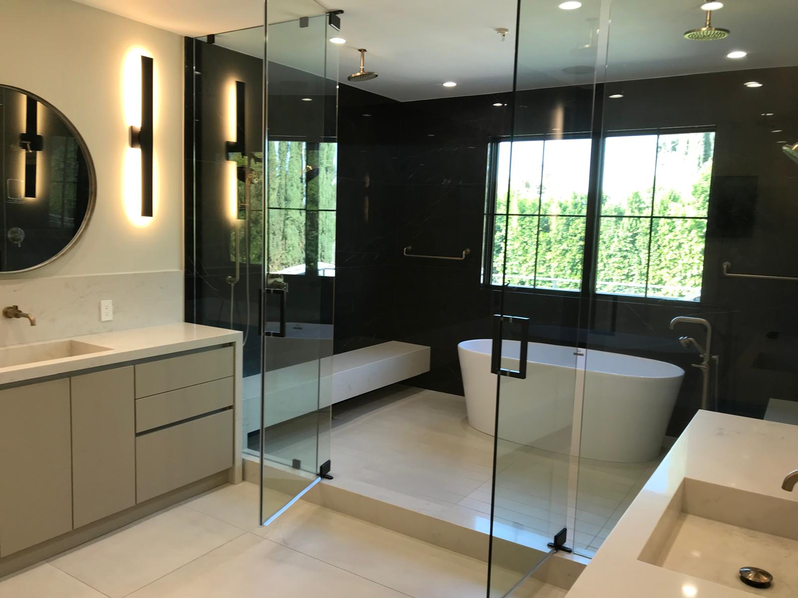 Modern luxury bathroom with white vanity, black tile shower, glass enclosure, freestanding tub, and contemporary lighting