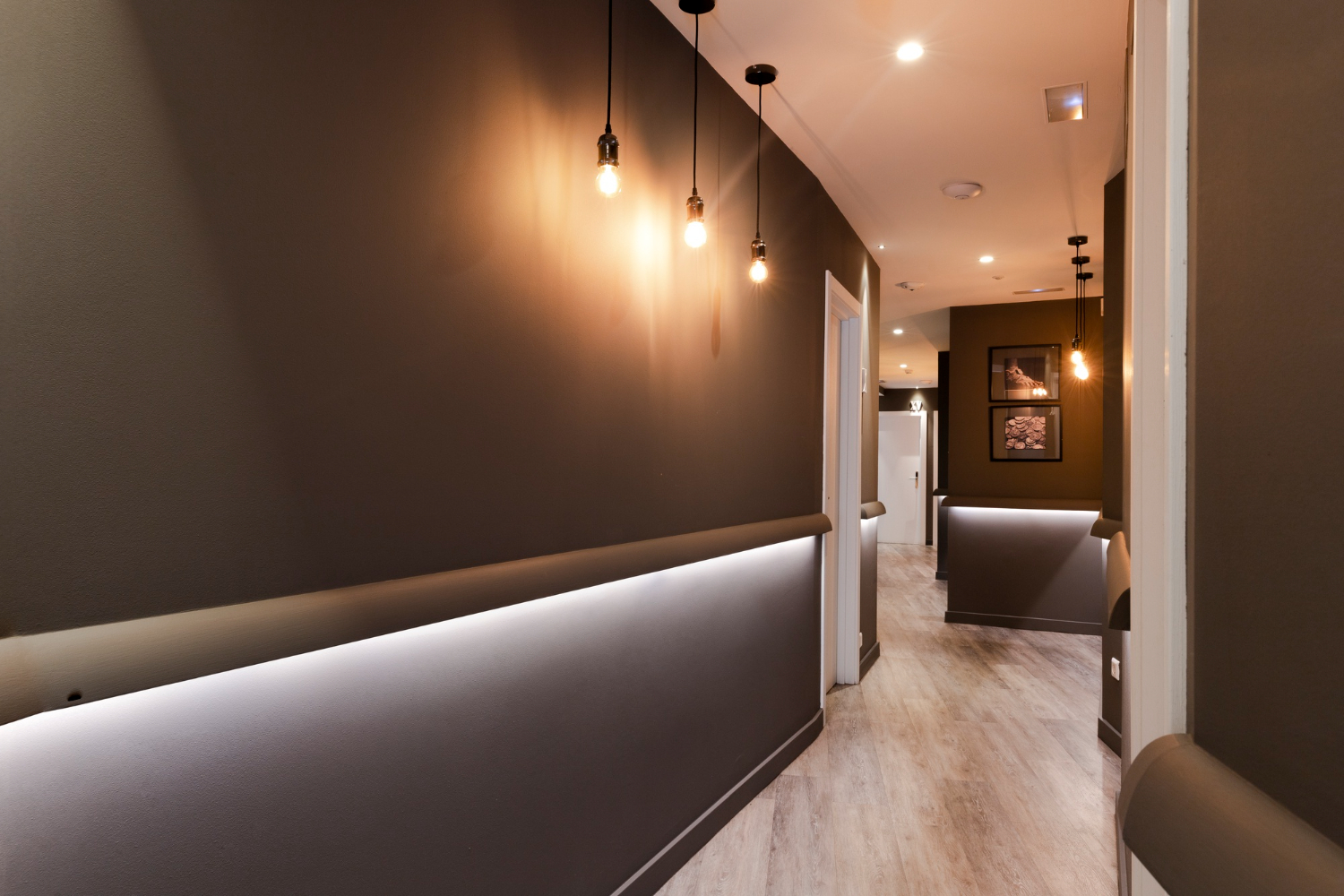 Modern restaurant interior with dark brown walls, pendant lighting, built-in banquette seating, and light wood flooring