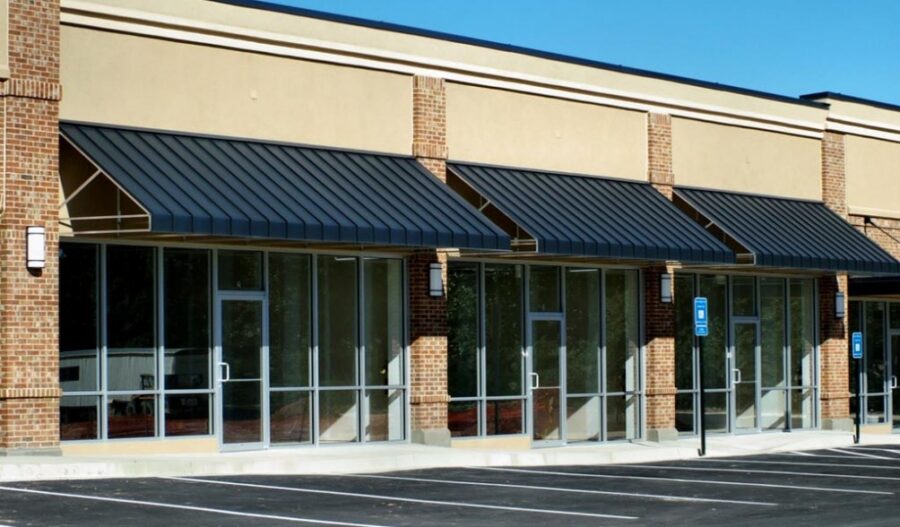 Modern commercial retail storefront with brick columns, metal awnings, and large glass windows in strip mall building